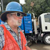 Construction worker in blue hard hat and orange safety vest near street sweeping truck