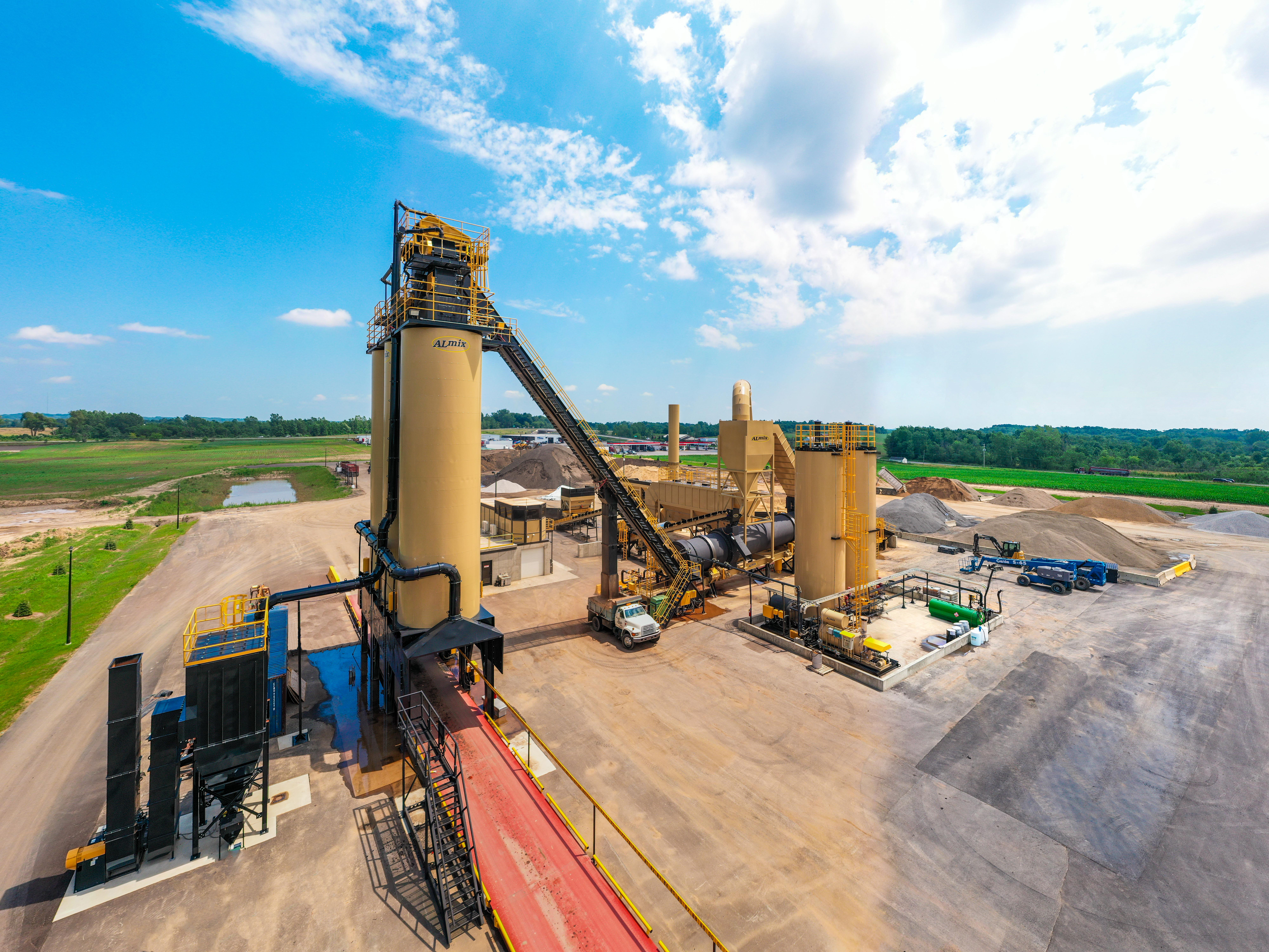 Industrial asphalt production facility with large yellow machinery under blue sky