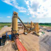 Industrial asphalt production facility with large yellow machinery under blue sky