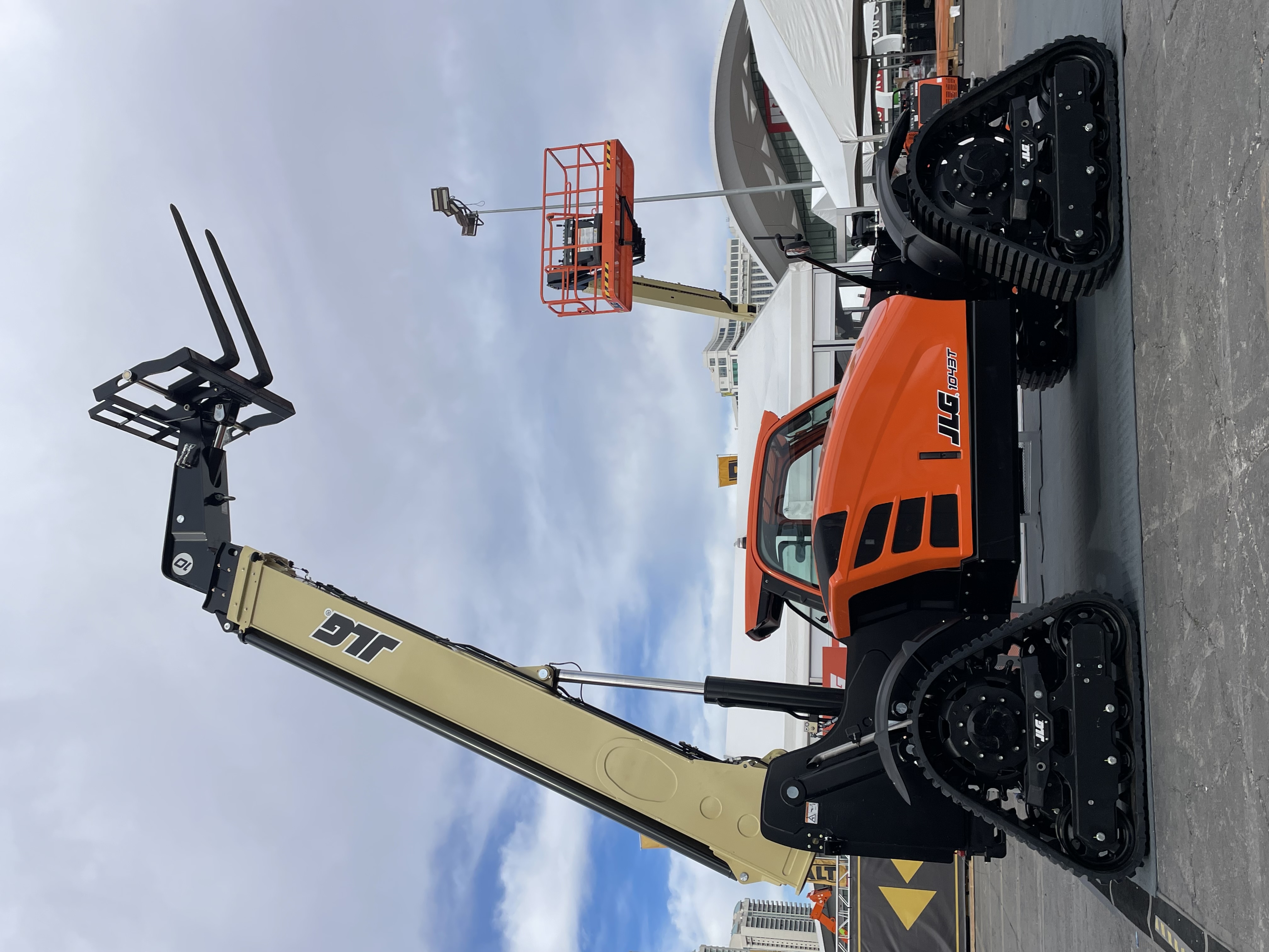 Orange JLG tracked telehandler with extended lifting arm at outdoor industrial event