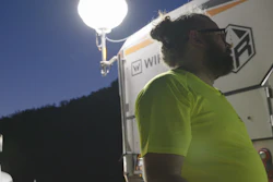 Worker in bright green shirt standing near illuminated vehicle at night