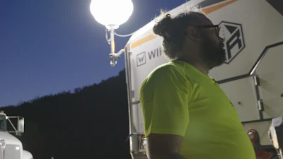 Worker in bright green shirt standing near illuminated vehicle at night