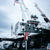 White mobile crane with extended boom and American flag on industrial site