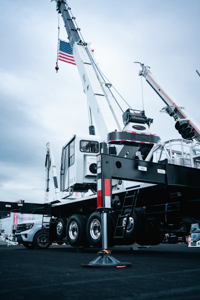White mobile crane with extended boom and American flag on industrial site