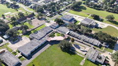 Aerial view of school campus with multiple buildings, trees, and green spaces