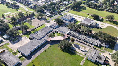 Aerial view of school campus with multiple buildings, trees, and green spaces