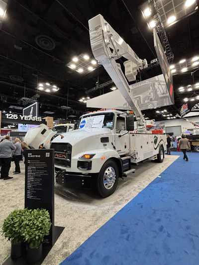 White commercial bucket truck with elevated lift displayed at industrial trade show exhibition booth