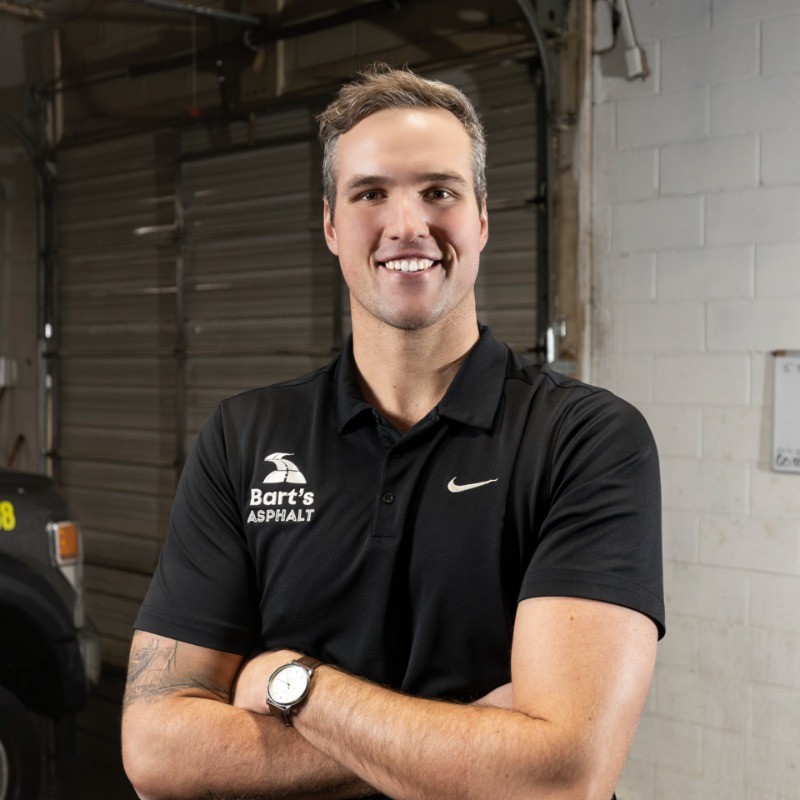 Smiling professional in black Nike and Bart's Asphalt polo shirt in industrial setting Headshot
