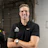 Smiling professional in black Nike and Bart's Asphalt polo shirt in industrial setting Headshot