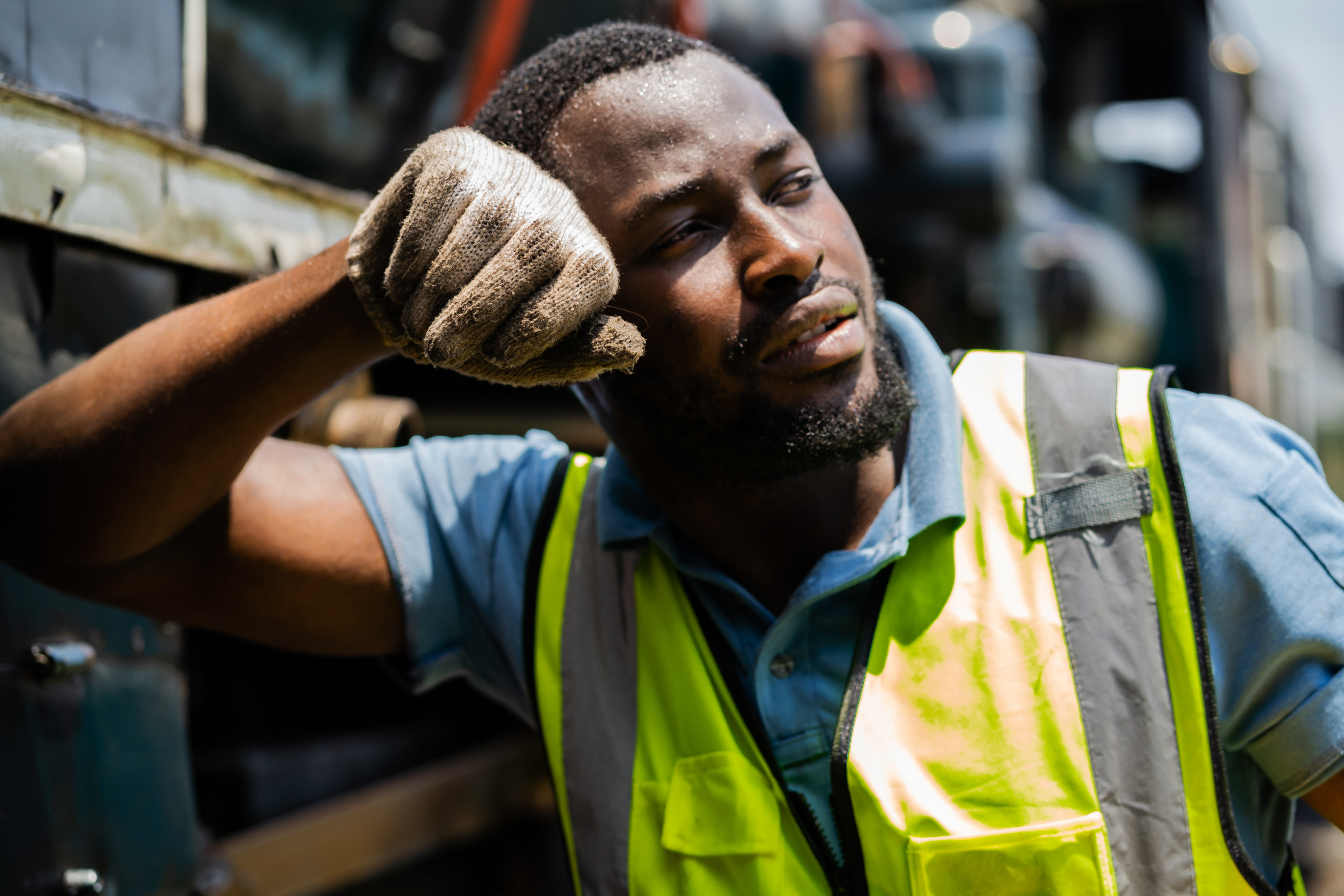 Fatigued construction worker in safety vest resting hand on head
