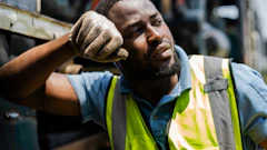 Fatigued construction worker in safety vest resting hand on head