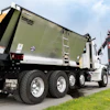 White and olive green commercial dump truck with Hawkeye Gold Group branding on highway with grain silo in background