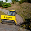 Yellow BOMAG road roller compacting dirt on a curved rural road