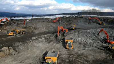 Construction site with orange excavators and dump trucks on rocky terrain