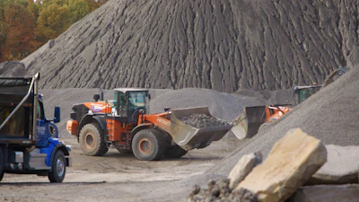 Orange wheel loader moving gravel near large stone piles at industrial quarry site