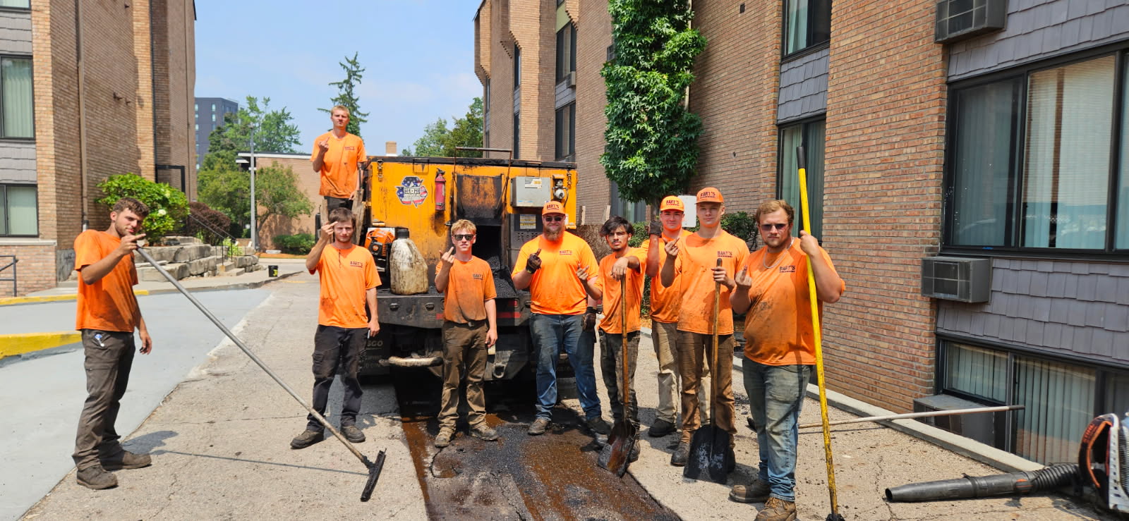 Construction crew in orange shirts repairing sidewalk next to brick buildings