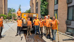 Construction crew in orange shirts repairing sidewalk next to brick buildings