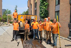 Construction crew in orange shirts repairing sidewalk next to brick buildings