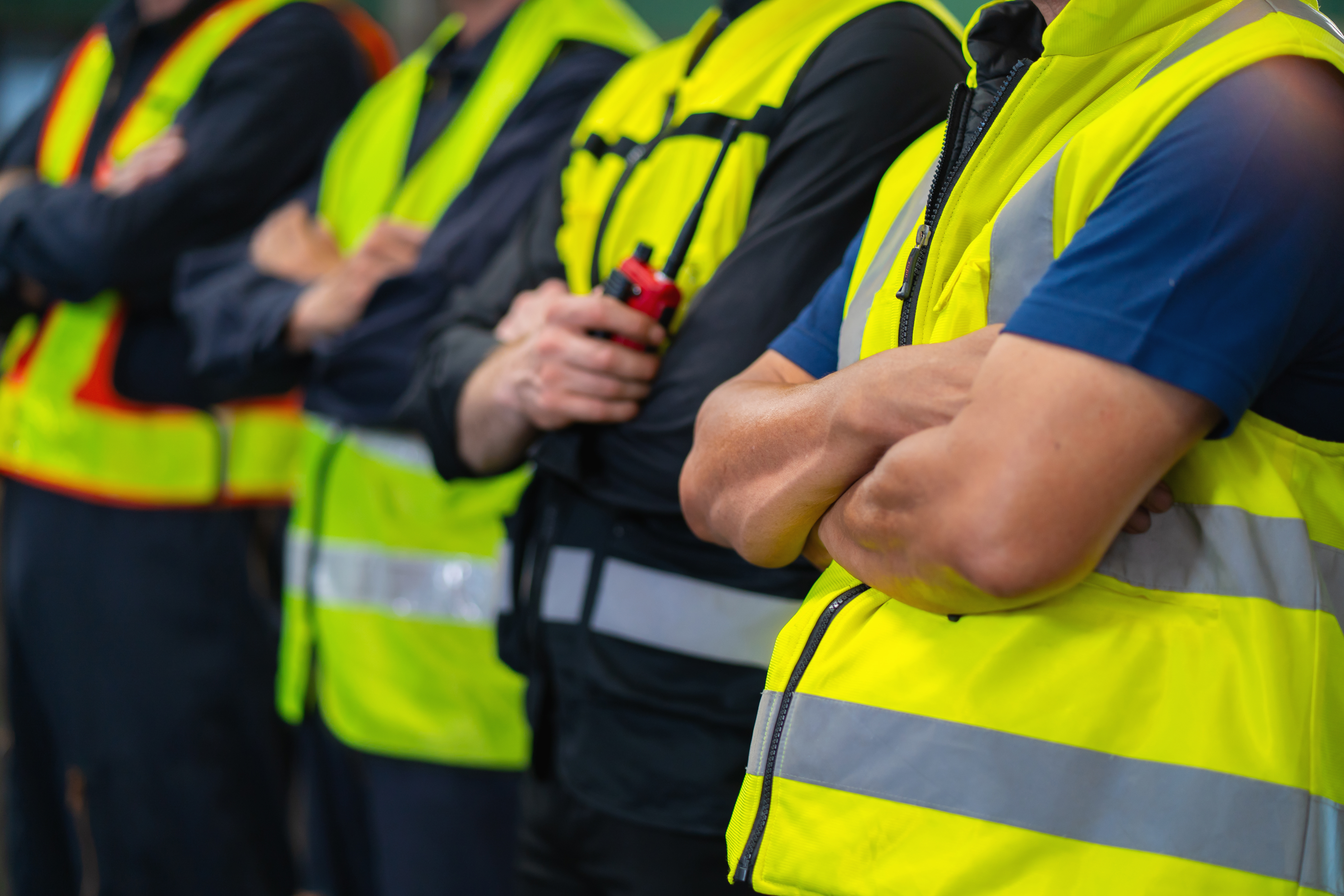 Workers in bright safety vests standing in formation with crossed arms