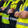 Workers in bright safety vests standing in formation with crossed arms