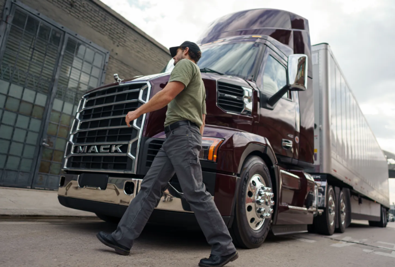 Professional truck driver walking beside maroon Mack semi-truck in urban loading area