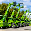 Green Merlo telehandlers lined up in a row with trees and blue sky background