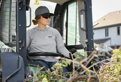 Worker in gray hoodie operating a construction vehicle among vegetation