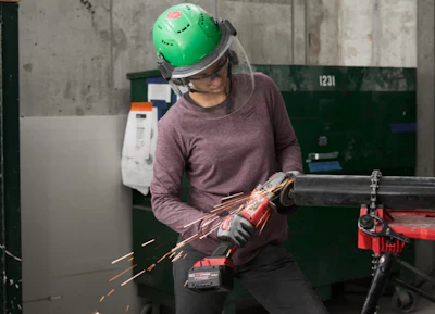 Worker in green safety helmet using angle grinder with sparks flying