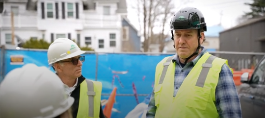 Two construction workers in safety gear discussing plans at a residential job site