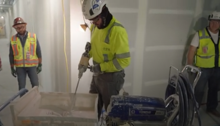 Construction workers in yellow safety vests installing drywall in an interior space
