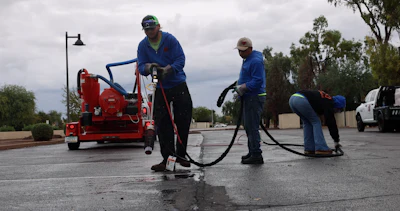 Workers using industrial cleaning equipment on wet asphalt parking lot