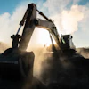 Excavator operating on dusty construction site with blue sky and clouds in background