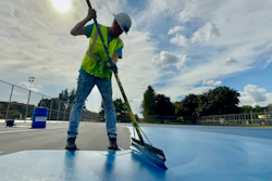 Construction worker in safety vest sweeping blue surface with push broom outdoors