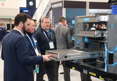 Professionals examine industrial 3D printing equipment at a technology trade show or conference event