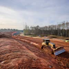 Yellow bulldozer grading red soil on hillside construction site with forested landscape and blue erosion control measures visible