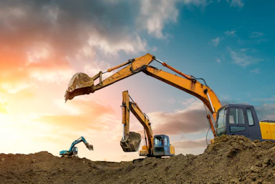 Heavy excavators operating on a construction site during golden hour with dramatic sky and earth mounds