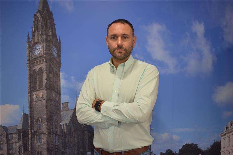 Man in light green shirt posing with arms crossed in front of historic clock tower Headshot