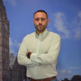 Man in light green shirt posing with arms crossed in front of historic clock tower