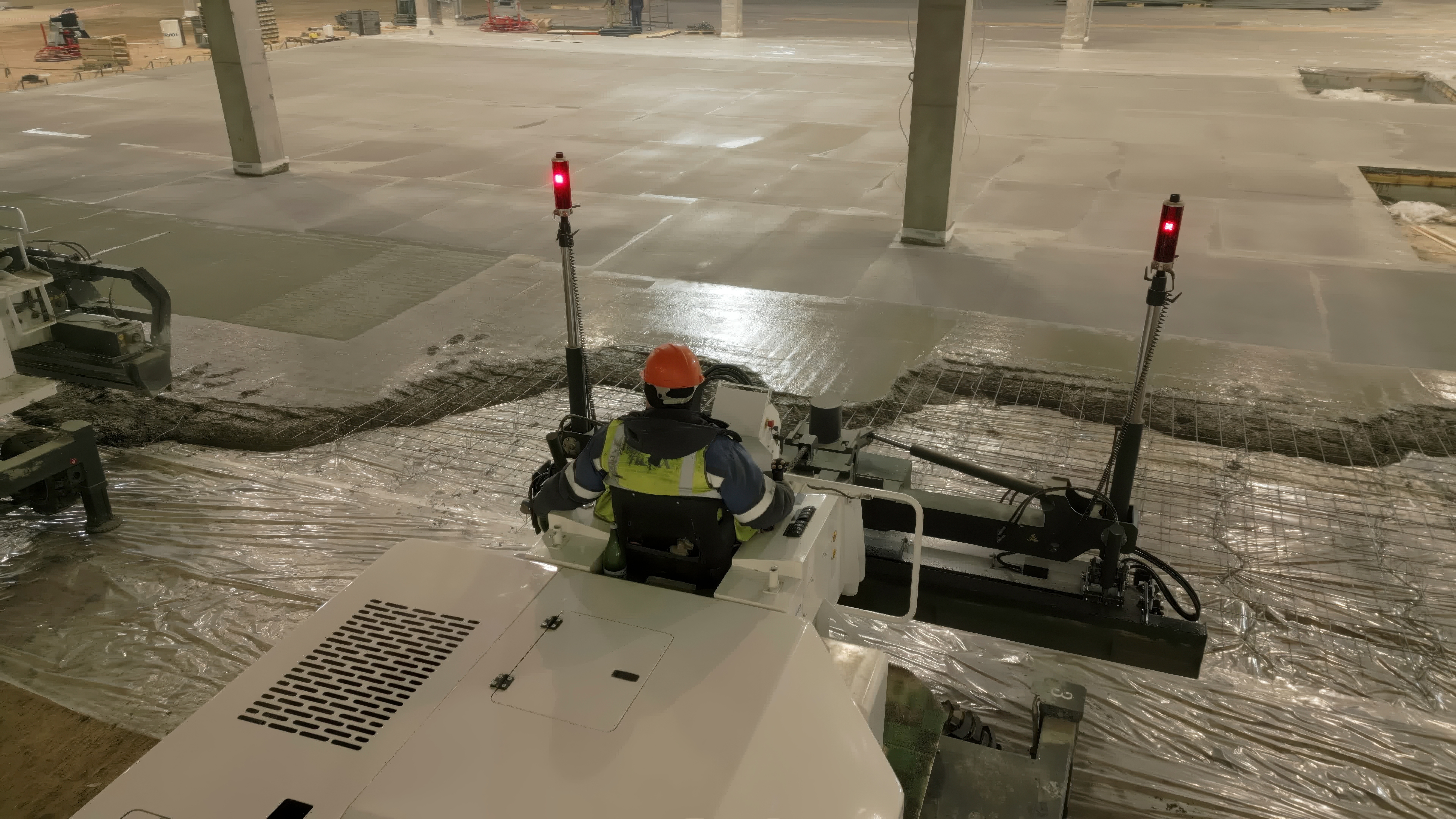 Construction worker in safety gear operating equipment in a parking garage with concrete pillars