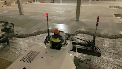 Construction worker in safety gear operating equipment in a parking garage with concrete pillars