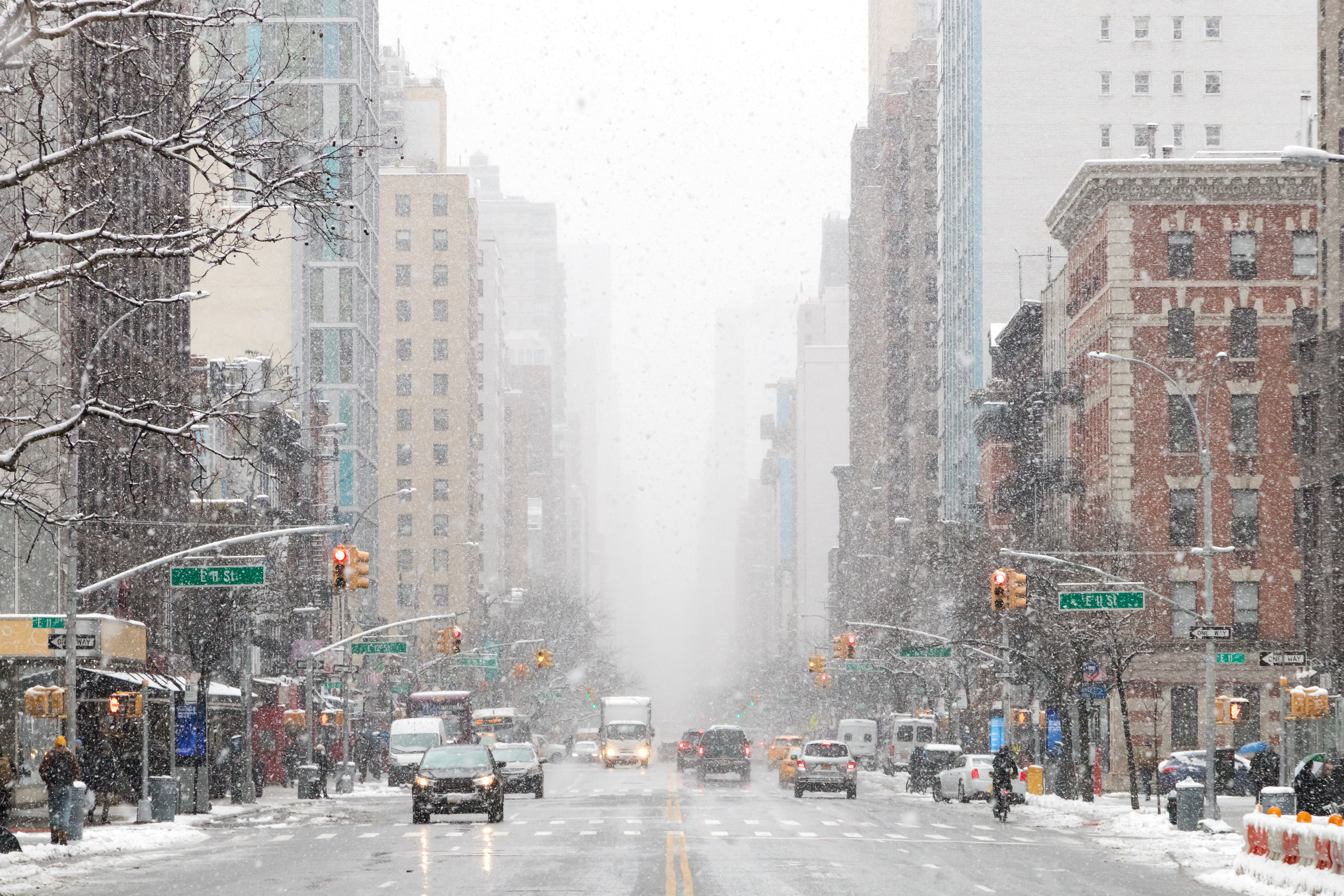 Snow-covered Manhattan street with tall buildings, yellow cabs, and traffic lights during winter weather