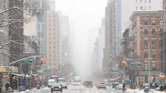 Snow-covered Manhattan street with tall buildings, yellow cabs, and traffic lights during winter weather