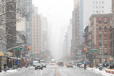 Snow-covered Manhattan street with tall buildings, yellow cabs, and traffic lights during winter weather