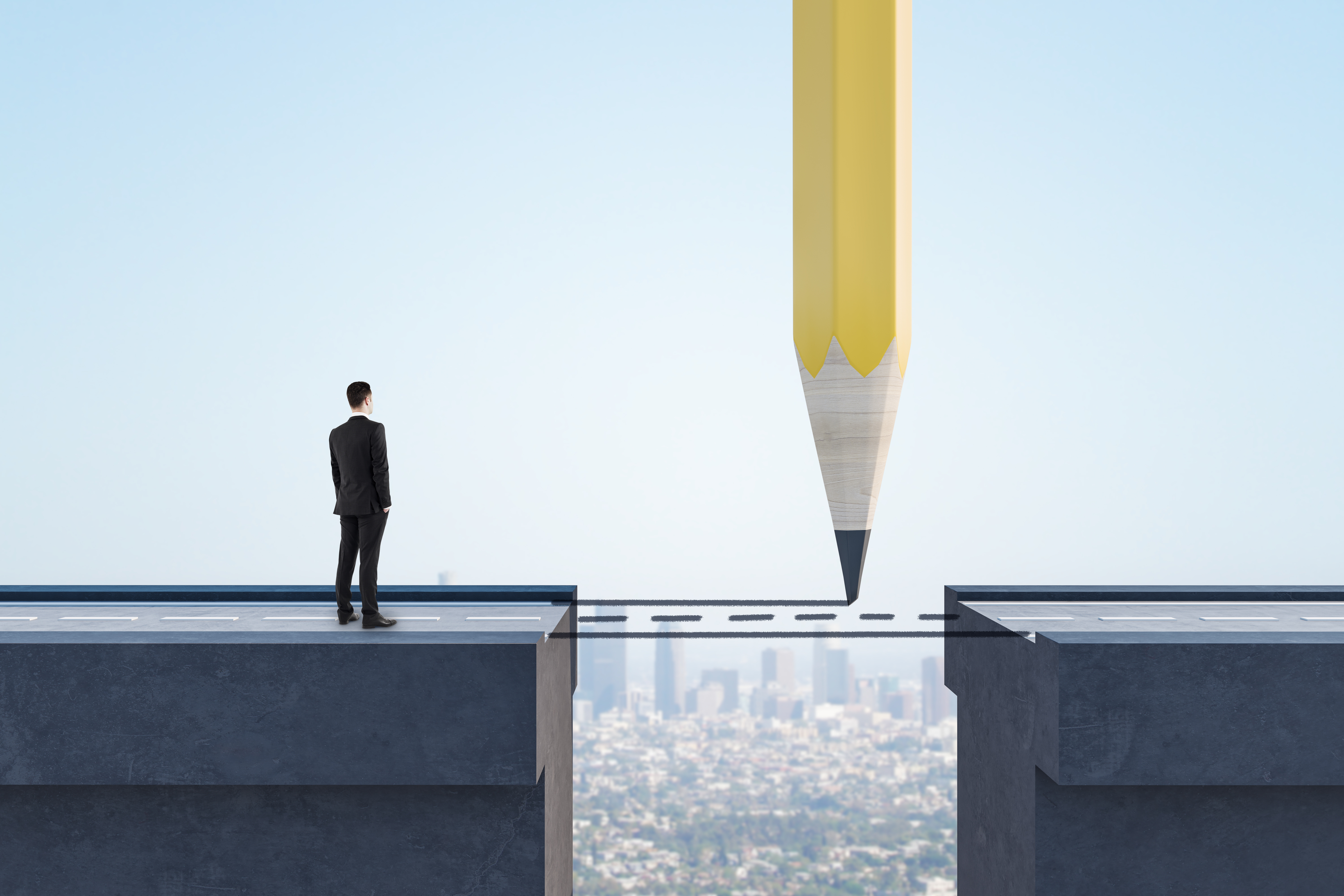 Businessman standing on cliff edge facing gap, with giant pencil drawing bridge to opposite platform above cityscape