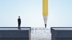 Businessman standing on cliff edge facing gap, with giant pencil drawing bridge to opposite platform above cityscape