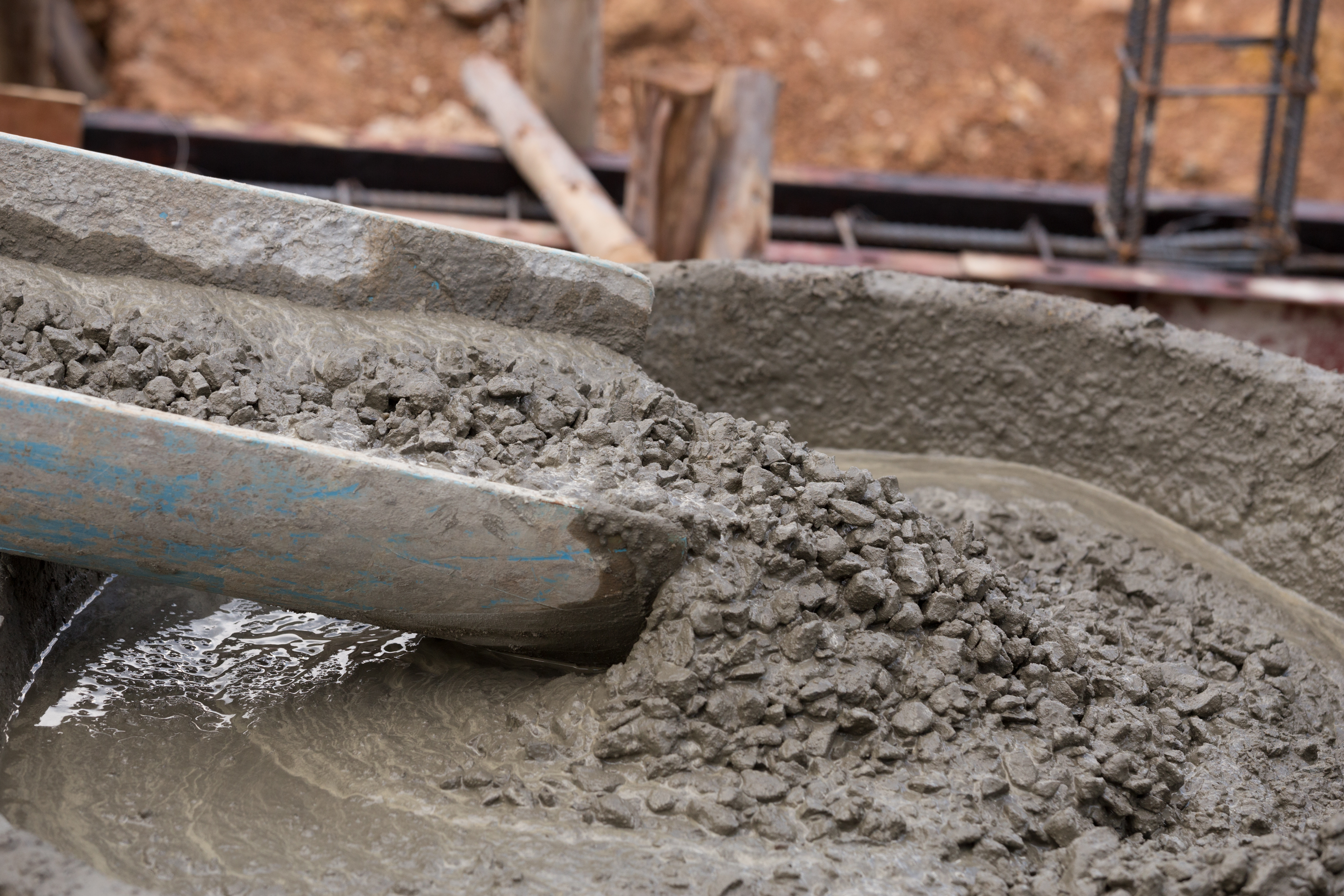 Worker mixing wet concrete with blue shovel at construction site