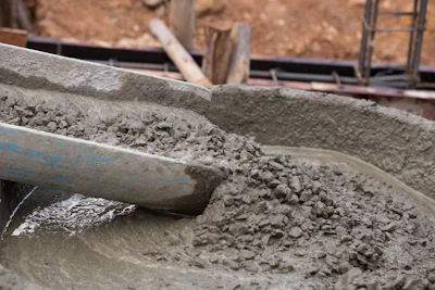 Worker mixing wet concrete with blue shovel at construction site