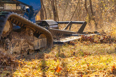 Wood chipper machinery covered in mulch and debris operating in a forest clearing during autumn.