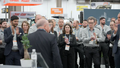 Business professionals applaud during a trade show or conference presentation in an industrial warehouse setting.