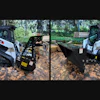 Two white Bobcat skid steer loaders with black bucket attachments on dirt ground in forest setting